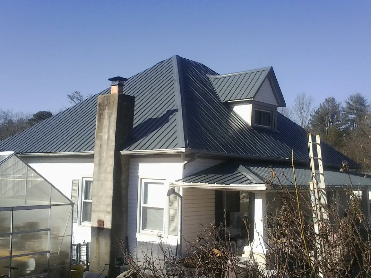 Dark blue standing seam metal roof on a white farmhouse with dormer — Slate & Tile Roof Repair by Roofing Brothers in Old Station