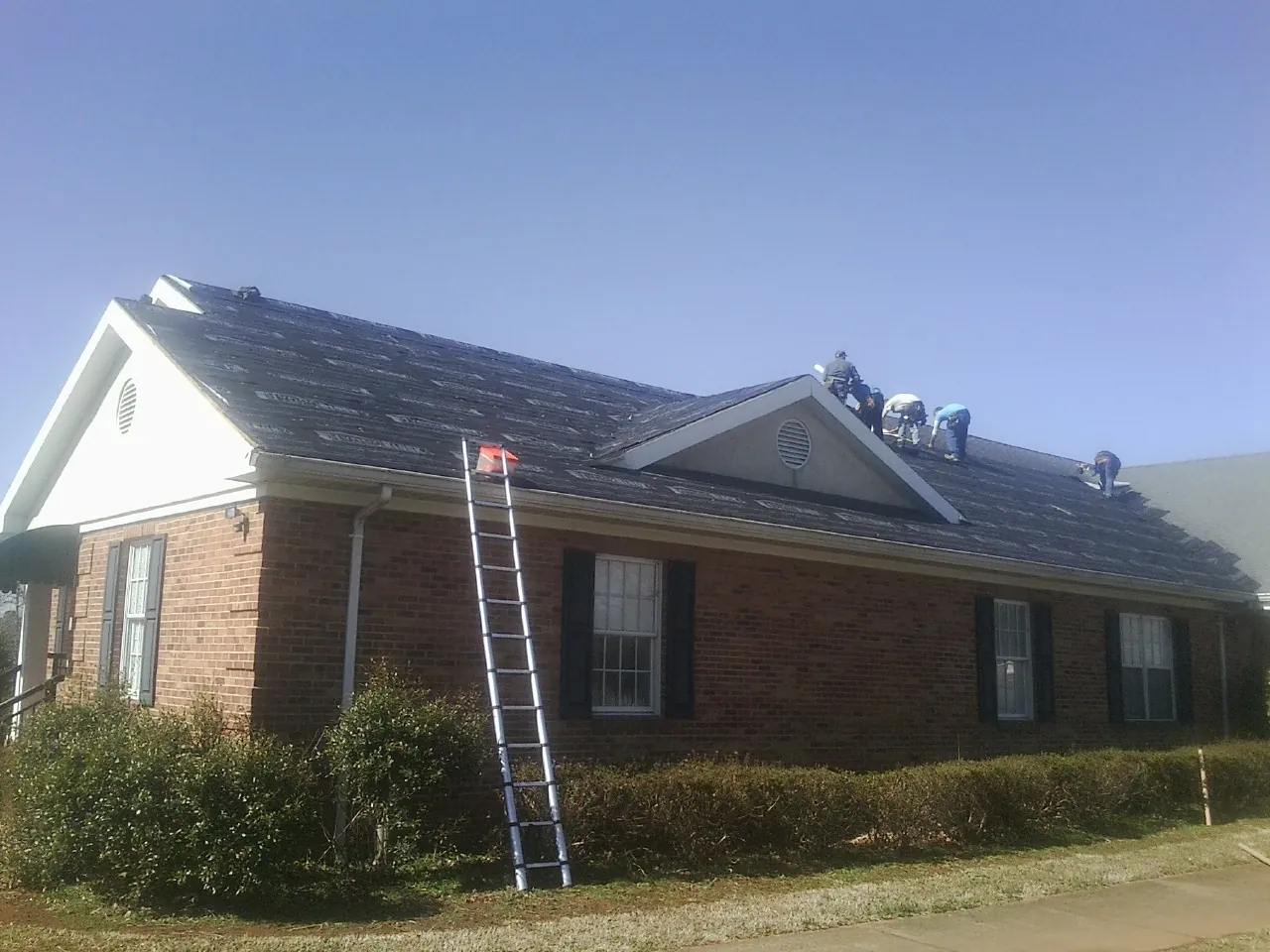 Crew tearing shingles off a brick ranch roof with a ladder set — Metal Roof Repair work by our crew in Old Station