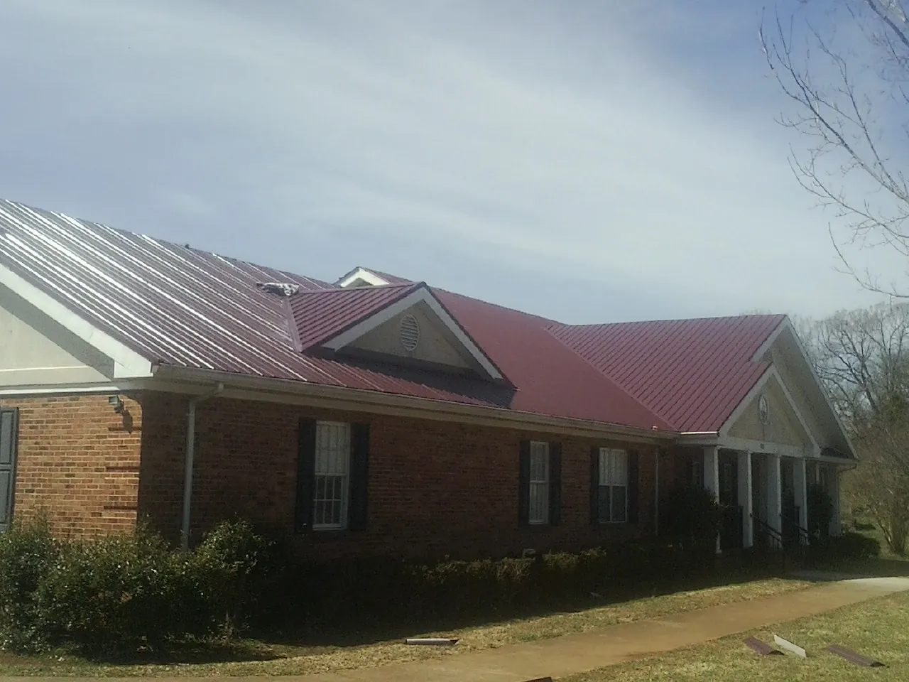 Red metal roof with gabled entries on a long brick building, from a Hail Damage Roof Repair job in Old Station