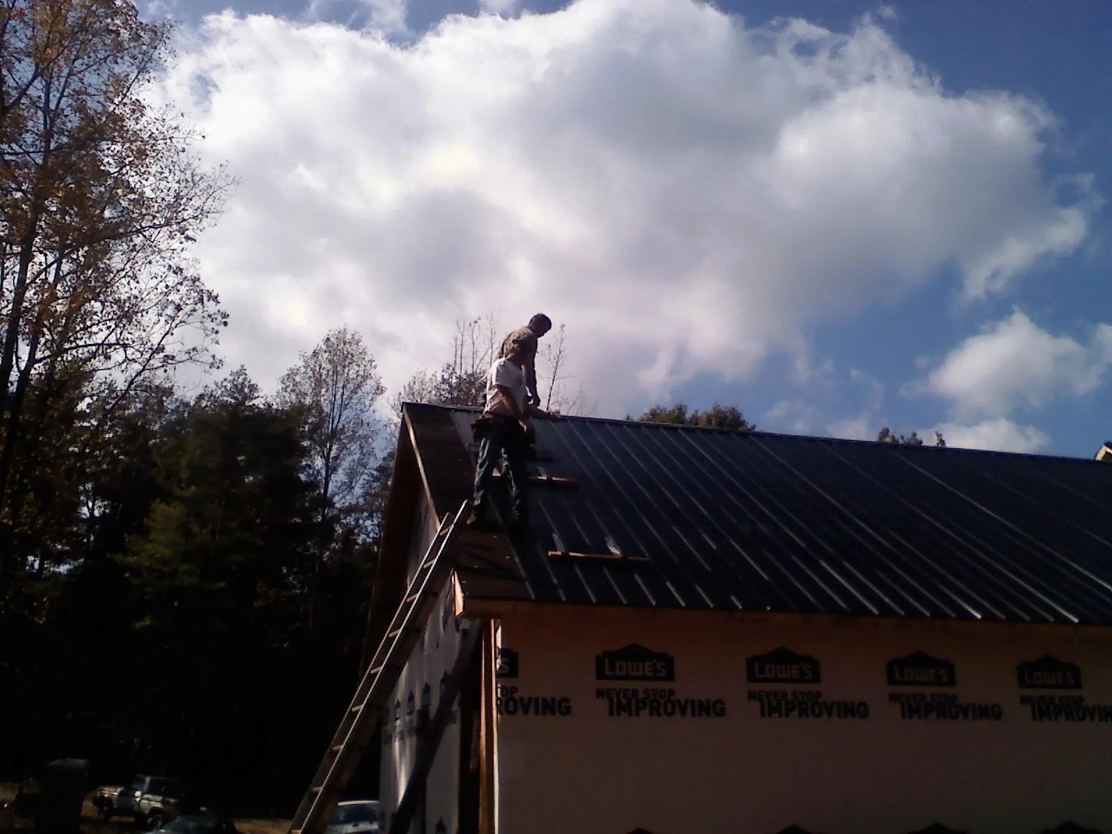 Roofer fastening dark metal panels high against a cloudy sky, from a Roof Inspection job in Old Station